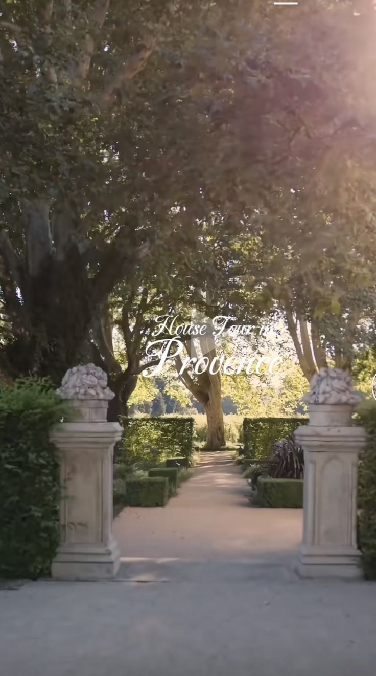 the sun shines brightly through the trees and bushes in front of an entrance to a formal garden