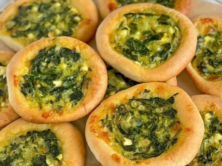 small pizzas with spinach and cheese are on a white plate, ready to be eaten