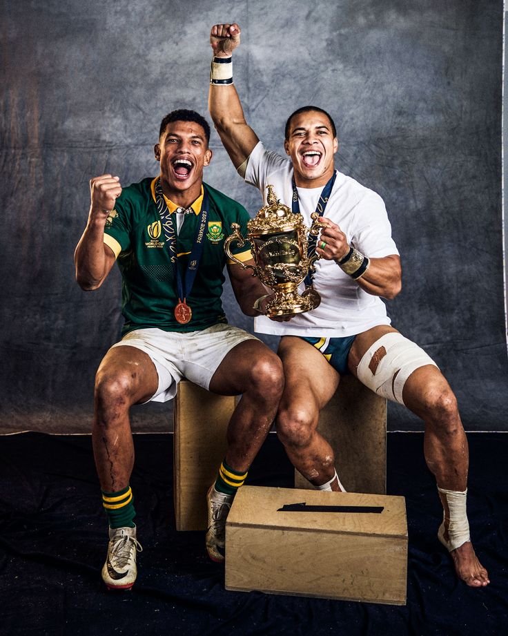 two men are sitting on a box and one is holding a trophy in his hand