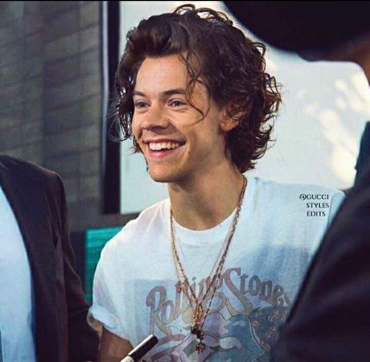 a man with curly hair is smiling and talking to another man wearing a white t - shirt