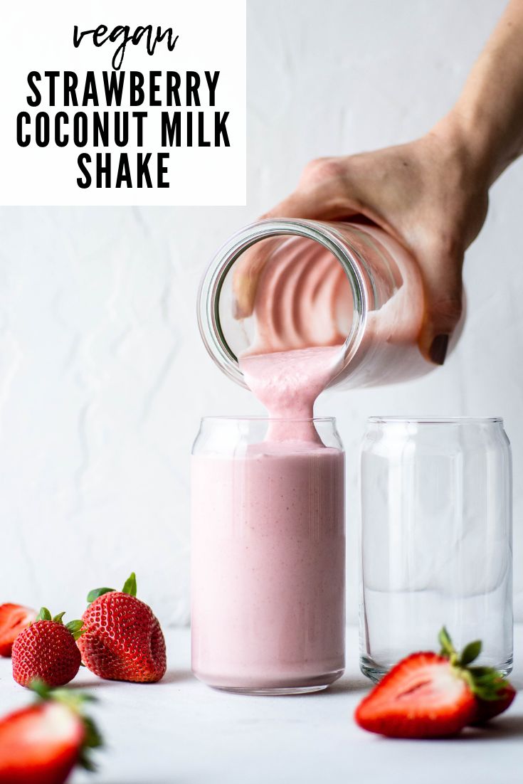 a person pouring milk into a jar with strawberries on the side