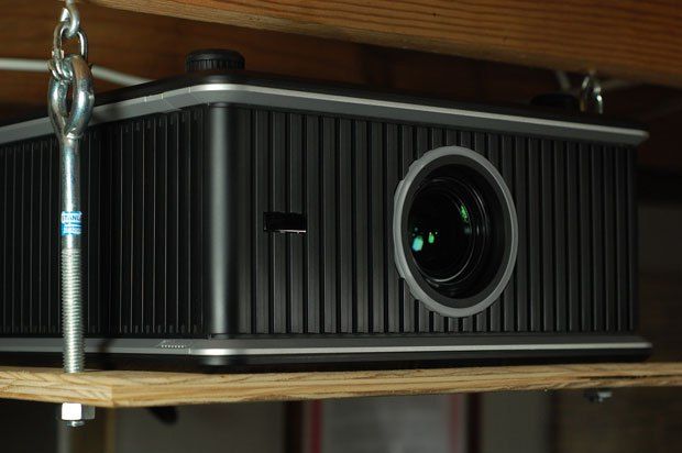 a black projector sitting on top of a wooden shelf next to a metal chain