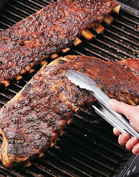 someone is grilling ribs on the grill with tongs in their hand and another person holding a spatula