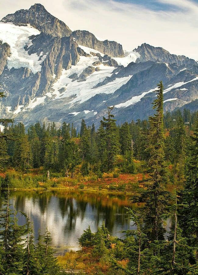 the mountains are covered in snow and surrounded by pine trees, with a small lake below