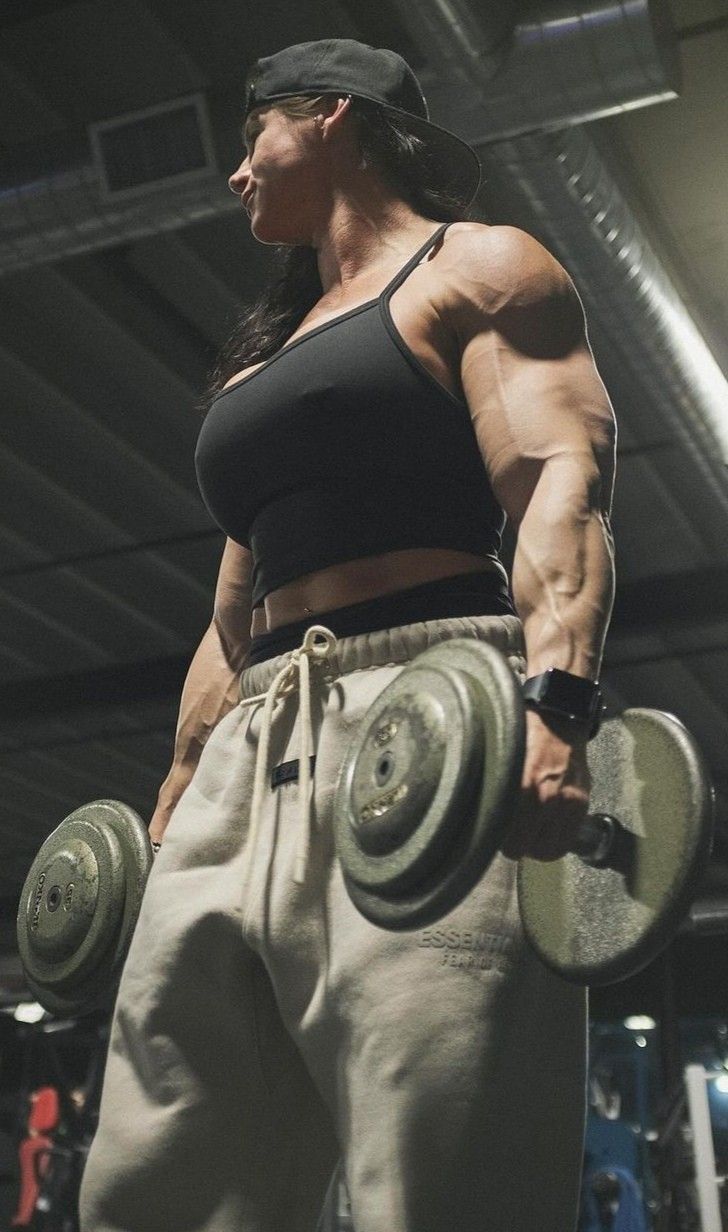 a female bodybuilde with two dumbs in her hands and one hand on his hip