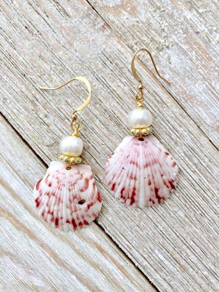 a pair of pink and white seashells with pearls are hanging from gold earwires