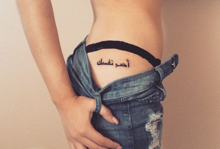 a woman's stomach with an arabic tattoo on her left side ribcage