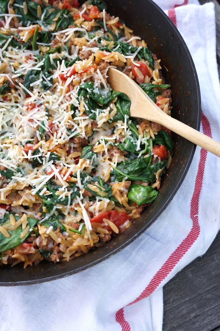 a skillet filled with pasta and spinach on top of a red and white towel