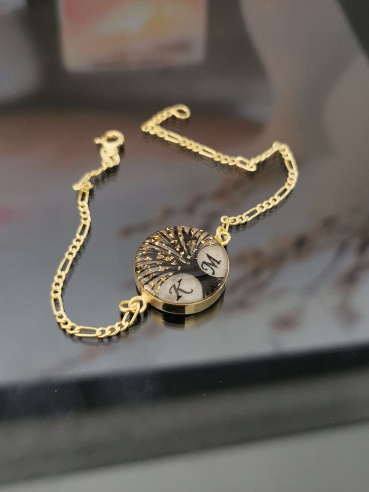 a gold chain bracelet with a clock and tree charm on the clasp, sitting on top of a table