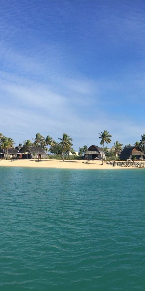 an island with palm trees and houses in the distance, seen from the water's edge