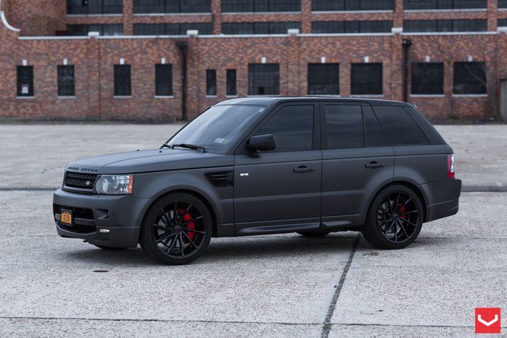 a grey range rover parked in front of a brick building with black rims and red accents