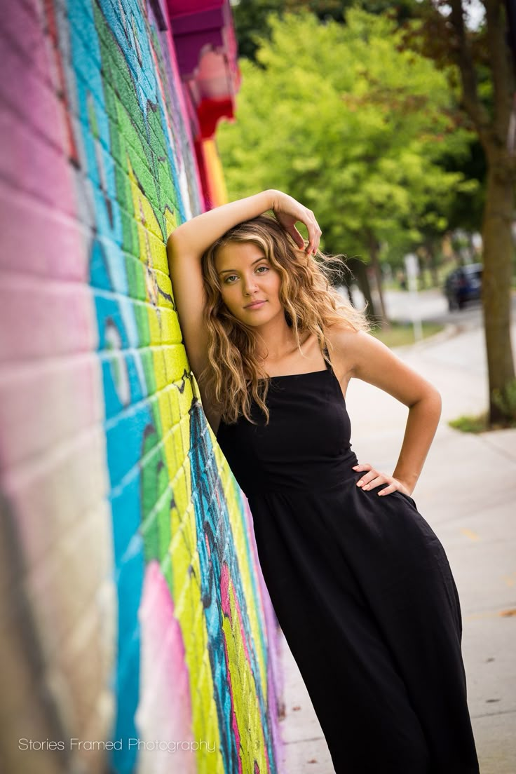 a beautiful young woman leaning against a colorful wall