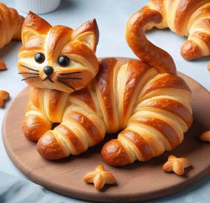 a pastry shaped like a cat sitting on top of a wooden plate next to other croissants