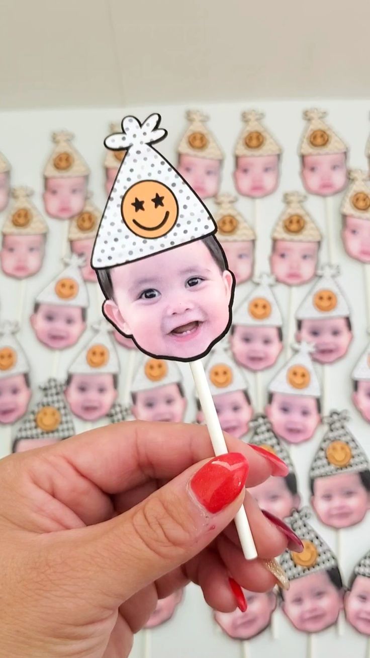 a person holding up a stick with a photo on it in front of a bunch of baby's faces