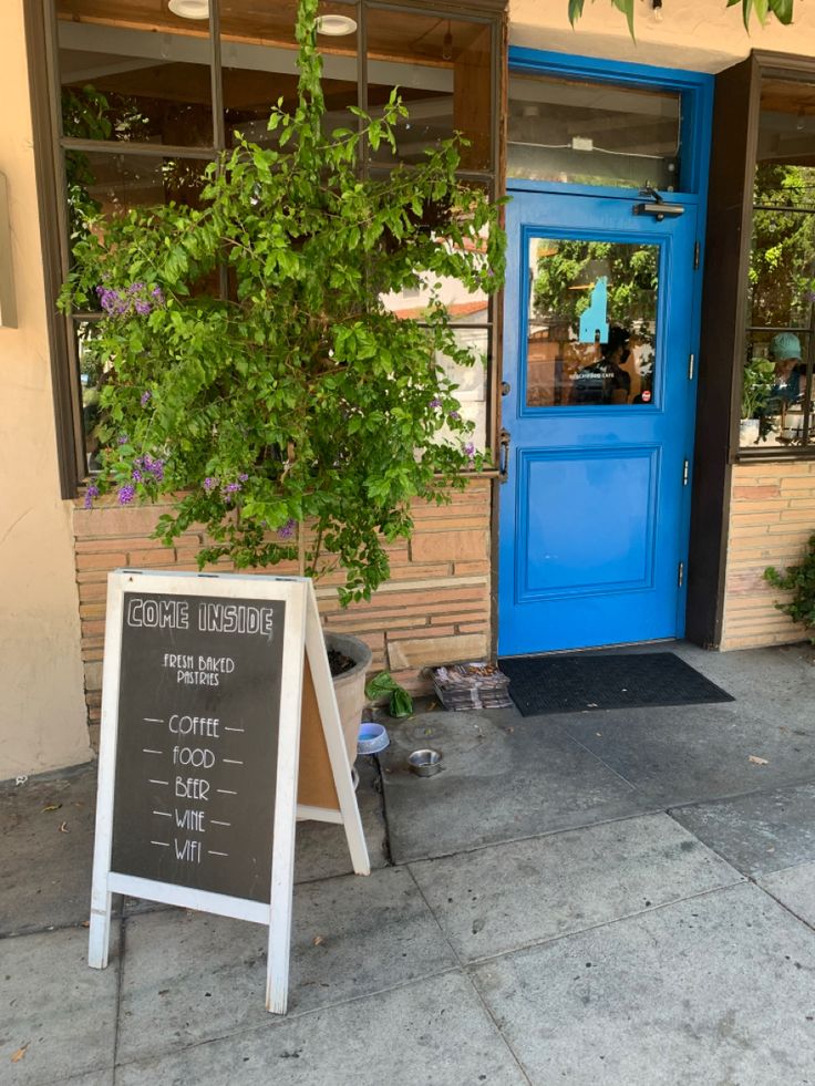 a blue door and sign in front of a building with plants on the sidewalk next to it