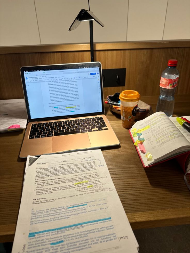 an open laptop computer sitting on top of a desk next to a book and cup