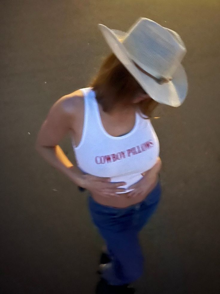 a woman in a white tank top and cowboy hat is standing on a skateboard