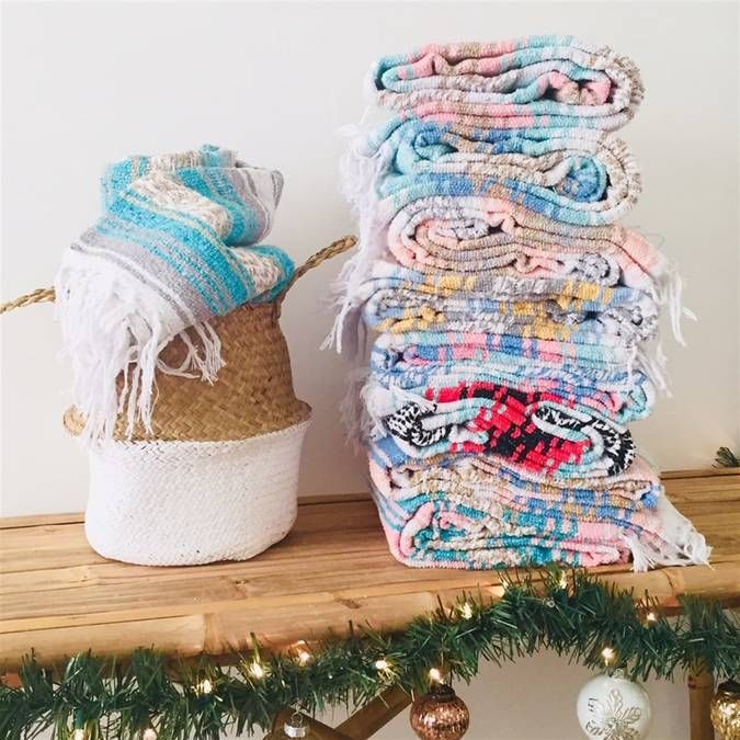 several blankets stacked on top of each other next to a basket with christmas lights in the background