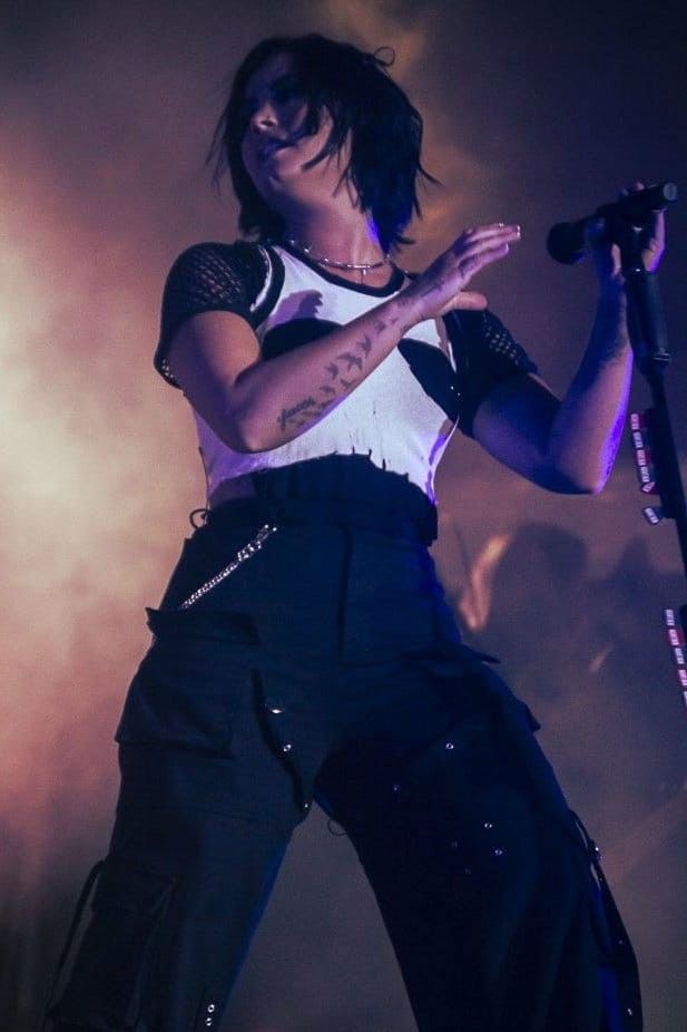 a woman standing on top of a stage holding a microphone in her hand and wearing black pants