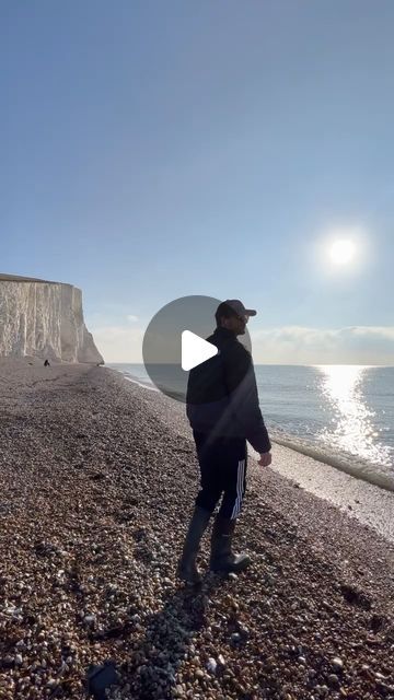 a man standing on top of a rocky beach next to the ocean under a blue sky