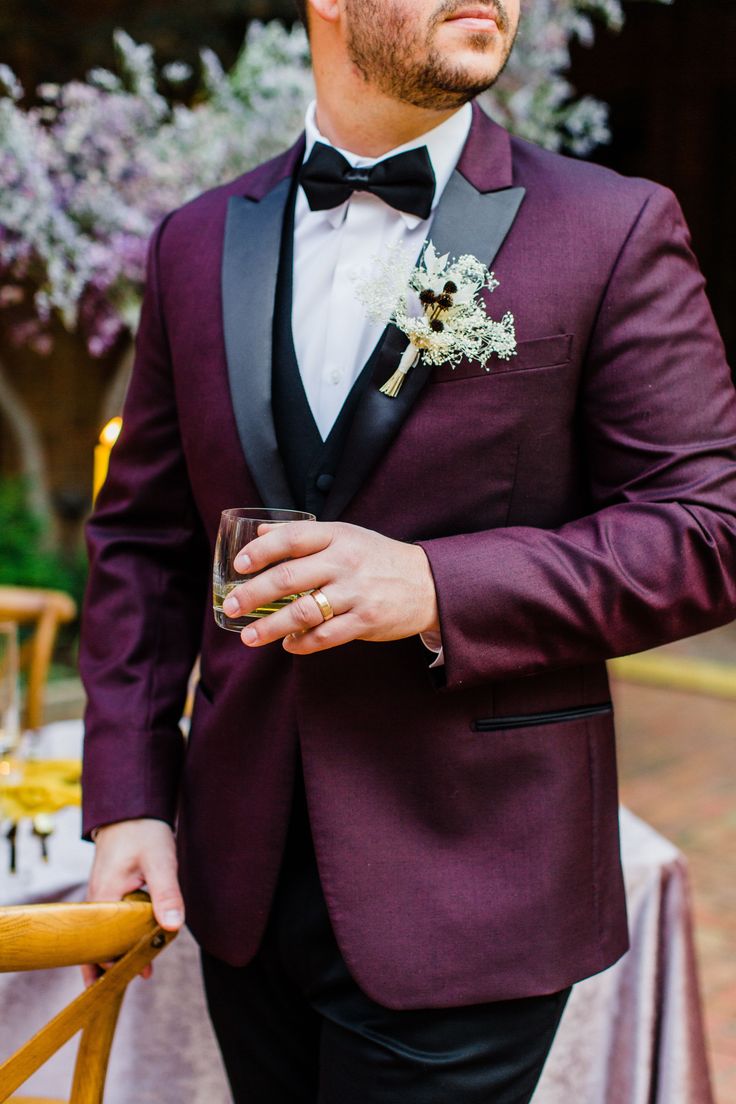 a man in a tuxedo standing next to a table with flowers and wine glasses