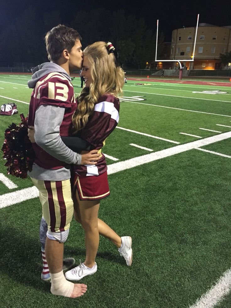 a man and woman standing on top of a football field with their arms around each other