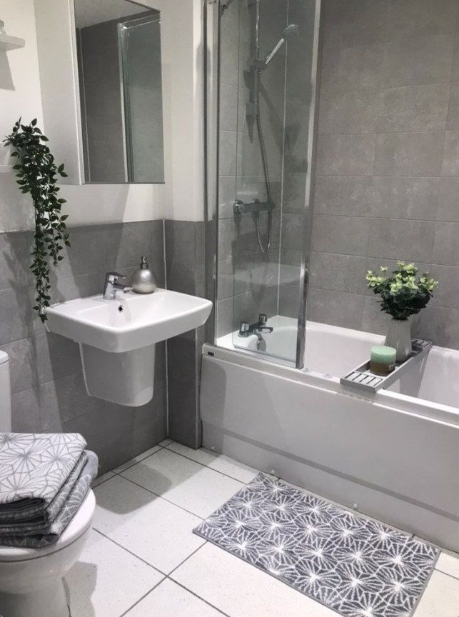 a white toilet sitting next to a bath tub under a bathroom mirror with plants in it