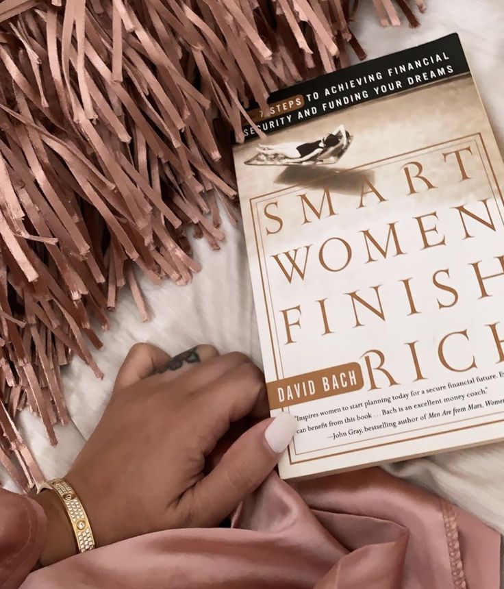 a woman is reading a book in bed with pink tassels on the wall behind her