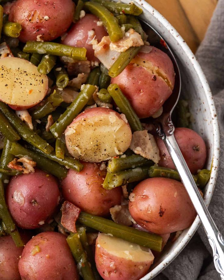 a bowl filled with potatoes and green beans on top of a table next to a fork