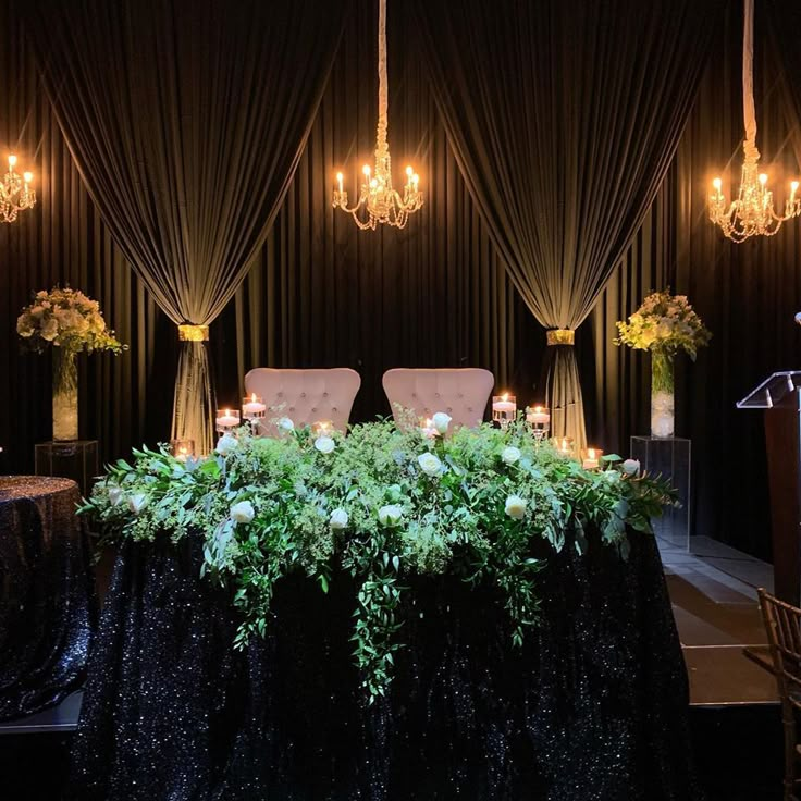 a table with flowers and candles on it in the middle of a room filled with black drapes