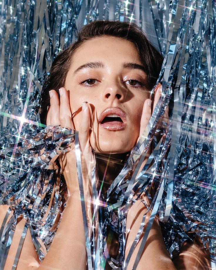 a woman with her hands on her face surrounded by shiny ribbons and streamers in the air