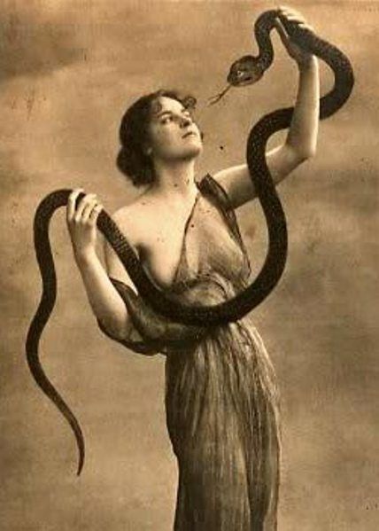 a woman holding a snake in her right hand and looking up at it's tail