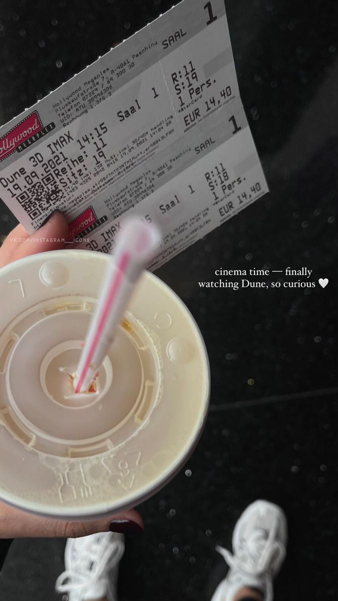 a person holding a cup with a straw in it and two tickets to the side