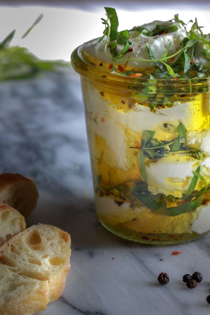 a jar filled with food sitting on top of a counter next to bread and herbs