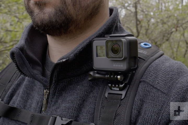 a man with a camera attached to his chest in front of some trees and bushes