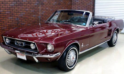 an old red mustang parked in front of a brick wall