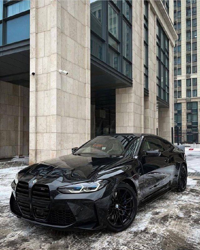 a black sports car parked in front of a building with snow on the ground and buildings behind it