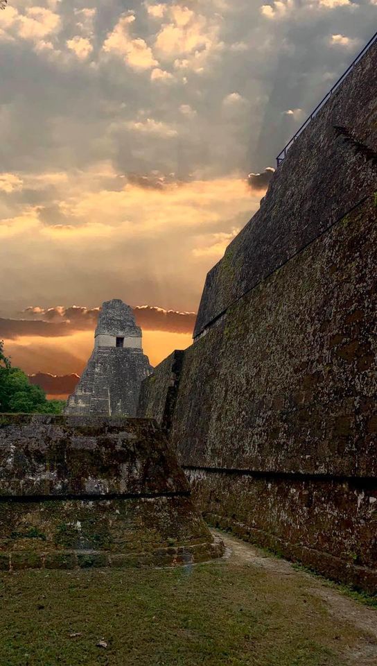 the sun is setting over some ruins in an ancient city with grass and trees on either side