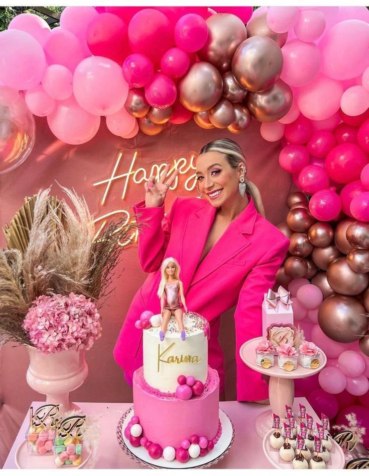 a woman standing in front of a pink and gold birthday cake