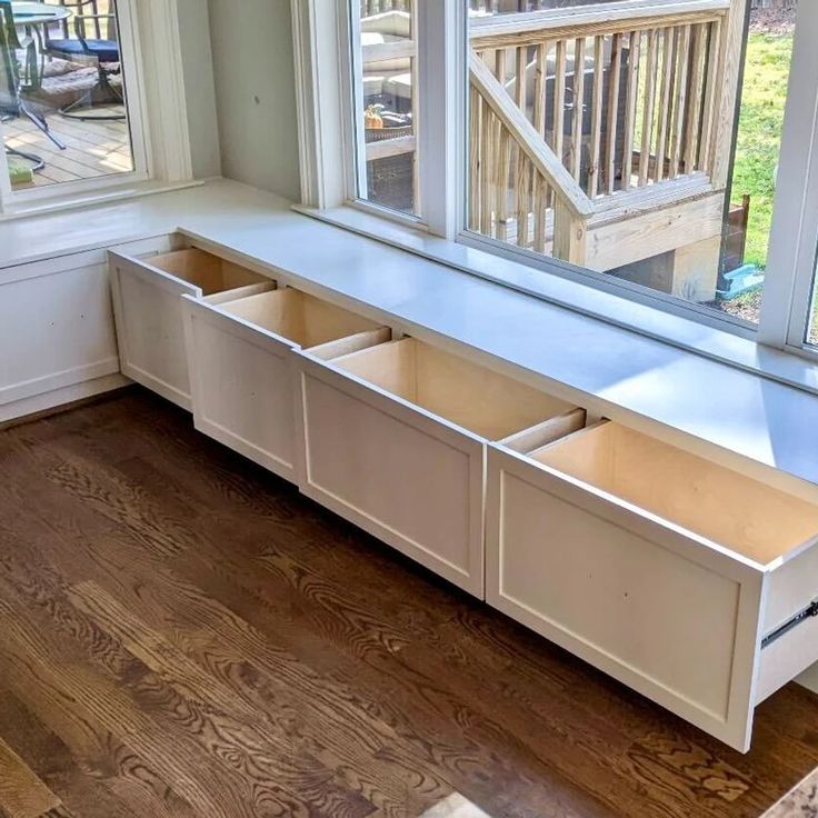 a window seat with two drawers in front of it on a hardwood floor next to windows