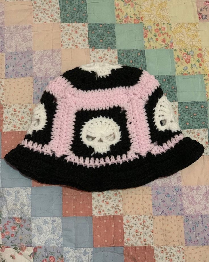 a crocheted black and pink hat sitting on top of a quilted blanket