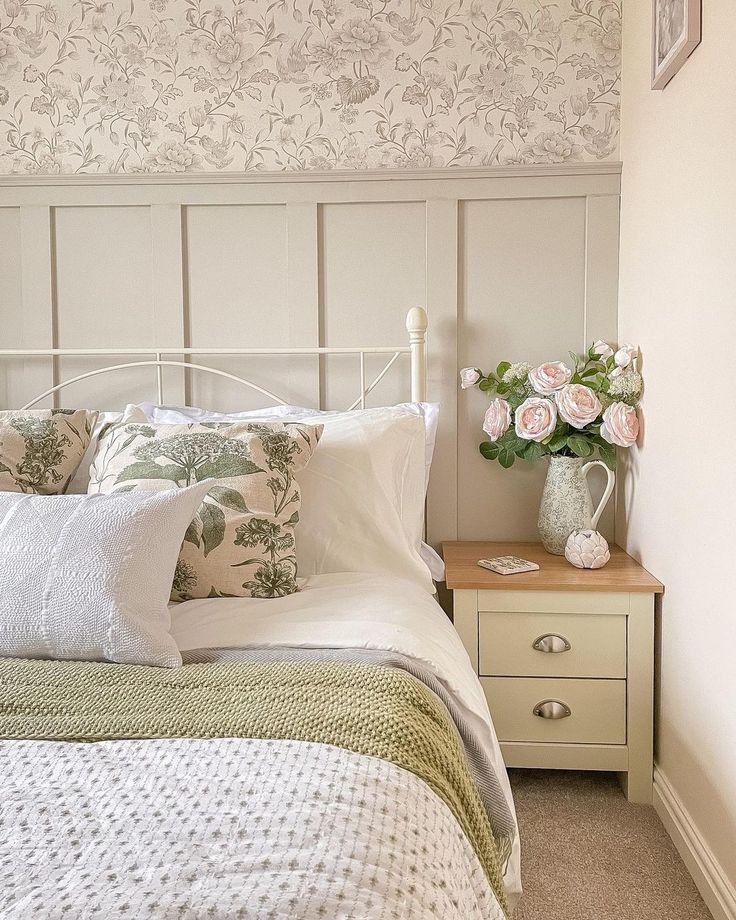 a white bed sitting next to a nightstand with flowers on it