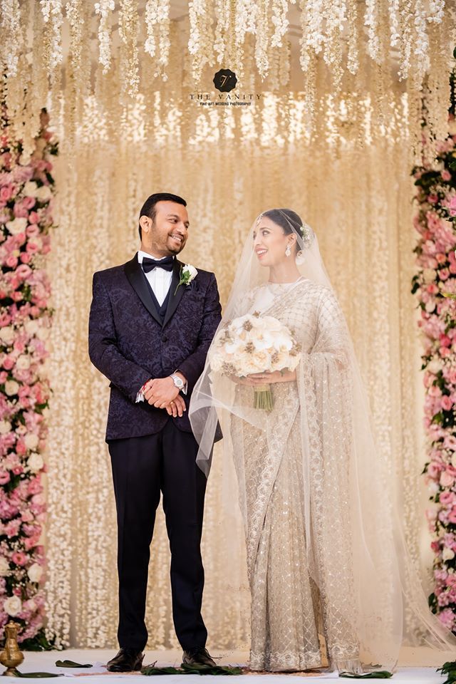 a man and woman standing next to each other in front of a flower covered wall