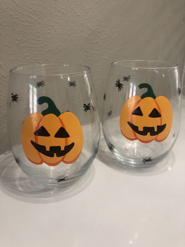 two glasses with pumpkin faces on them sitting next to each other in front of a white wall