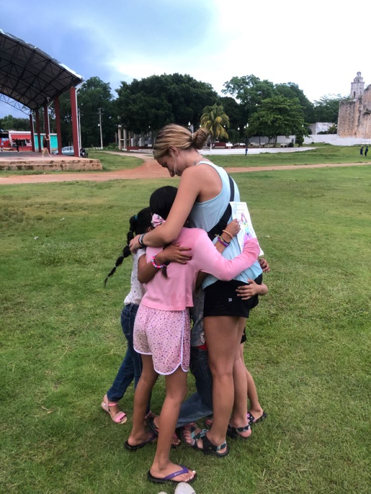 a group of people standing around each other in the grass with their arms around one another