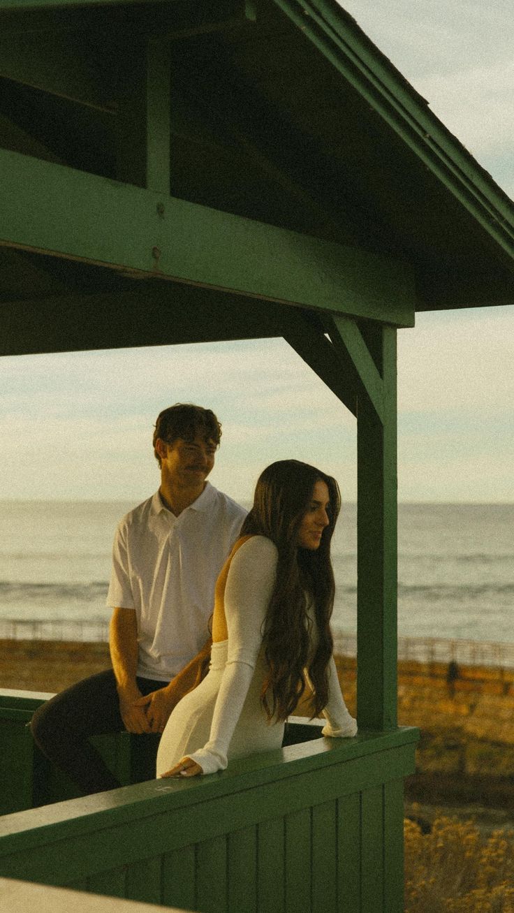 a man and woman sitting next to each other on a bench near the ocean in front of them