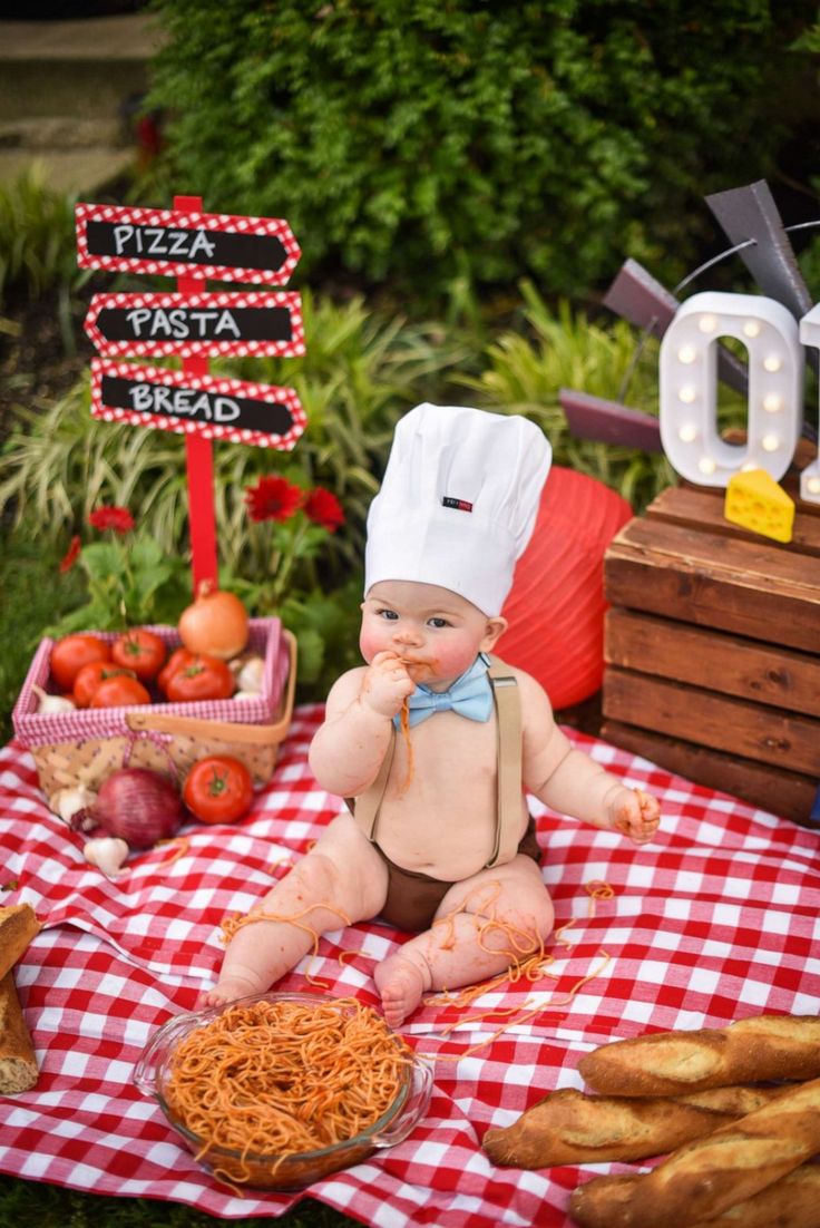 a baby sitting on a red and white checkered table cloth with food in front of it