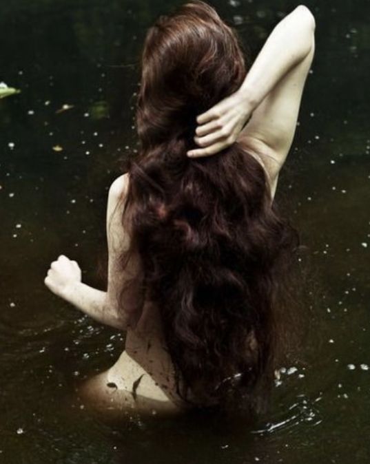 a woman is sitting in the water with her back to the camera and arms behind her head