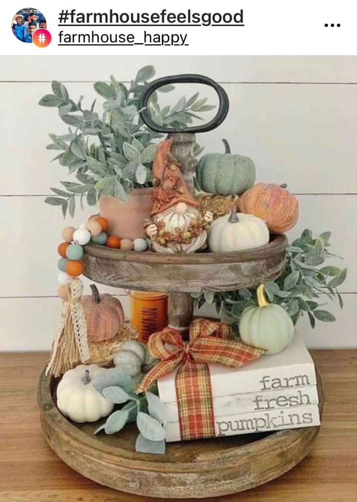 a three tiered tray with pumpkins and gourds on it, sitting on top of a wooden table