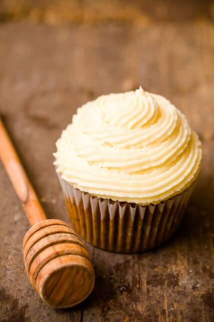 a cupcake sitting on top of a wooden table next to a wooden spoon and honey stick